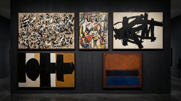 A wide-angle view of a modern gallery wall painted in dark charcoal gray, displaying five famous Abstract Expressionist paintings framed in dark wood and arranged in an aligned grid layout. Top Row: On the left, a dense drip painting by Jackson Pollock in beige, black, and white; in the middle, Willem de Kooning's expressive, semi-abstract figure painting featuring bold brushstrokes and vibrant red and yellow accents; on the right, Franz Kline's stark black-and-white composition of thick, architectural strokes. Bottom Row: On the left, Robert Motherwell's Elegy to the Spanish Republic motif featuring black ovoid and vertical forms on a beige and ochre background; on the right, Mark Rothko's color-field painting with glowing stacked rectangular bands of rust-orange, black, and deep blue.