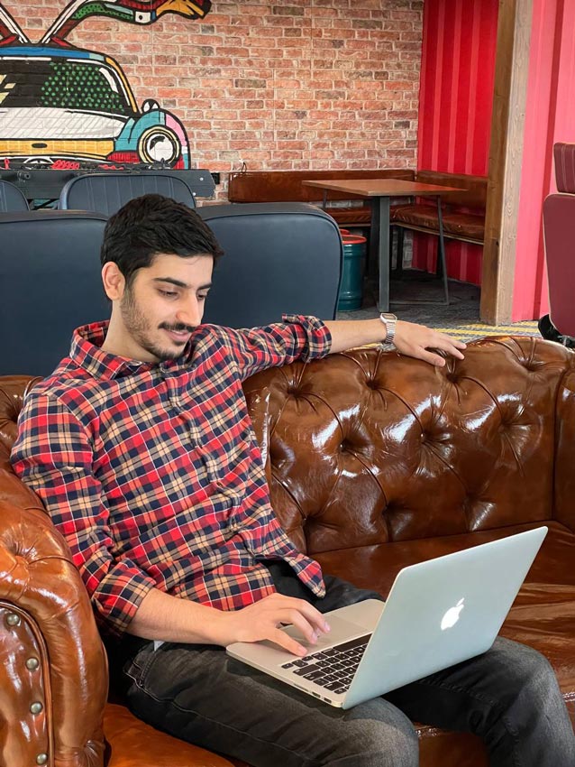 a man sitting on brown Chester sofa with laptop on his lap